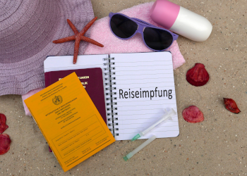 Pass, Impfausweis und Sonnenbrille liegen am Strand